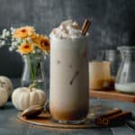Homemade iced pumpkin spice latte in tall glass topped with whipped cream, cinnamon, and cinnamon stick.