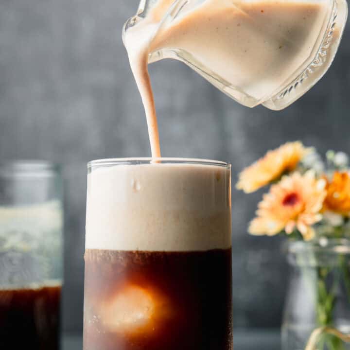 Pumpkin cream cold foam pouring over a tall glass of iced cold brew coffee.