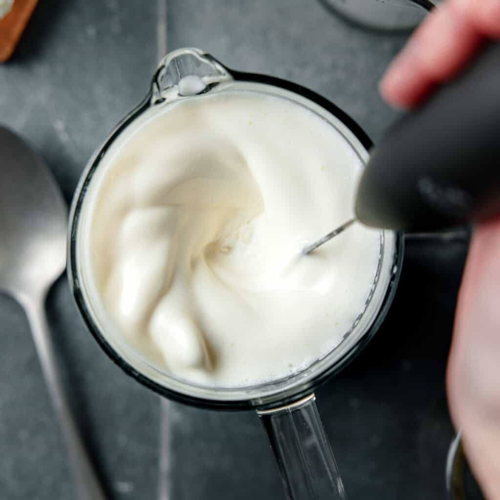 A frother mixing the vanilla sweet cream in measuring cup.