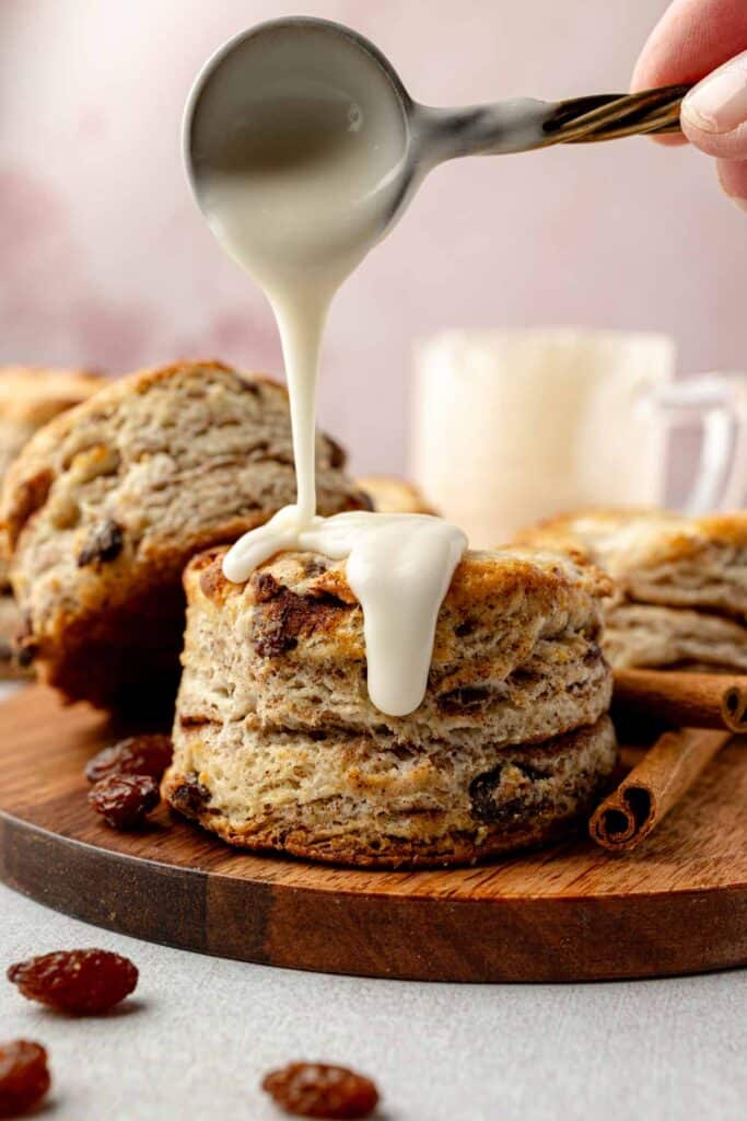 Icing dripping from spoon onto top of gluten-free cinnamon raisin biscuits.