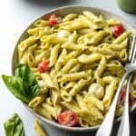 Pasta with creamy pesto sauce in large bowl with tomatoes and mozzarella cheese balls.