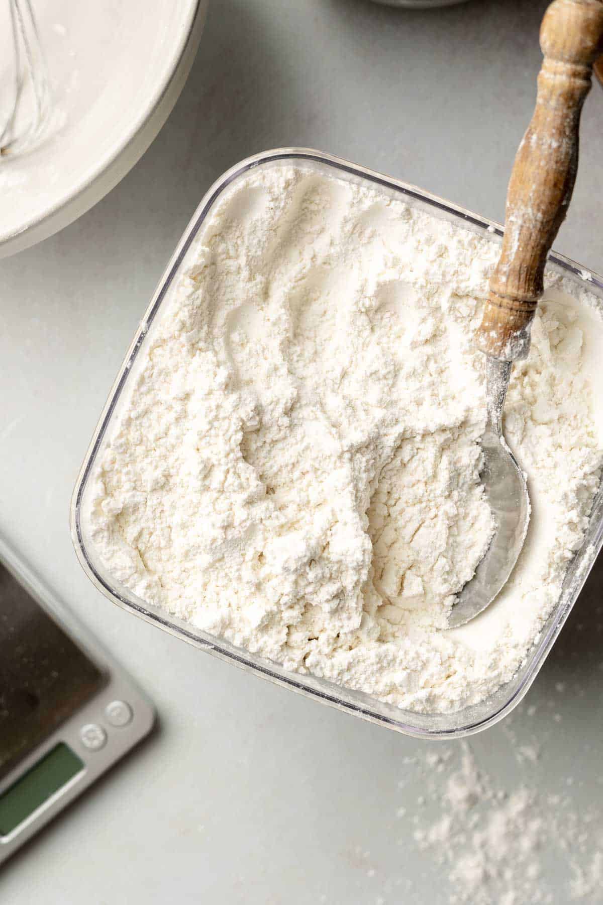 Flour bin filled with cup4cup original multipurpose gluten-free flour blend and wooden spoon handle sticking out.