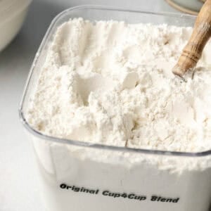 A bin filled with cup4cup gluten-free flour blend, wooden spoon handle sticking out.