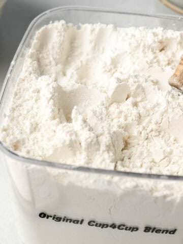 A bin filled with cup4cup gluten-free flour blend, wooden spoon handle sticking out.