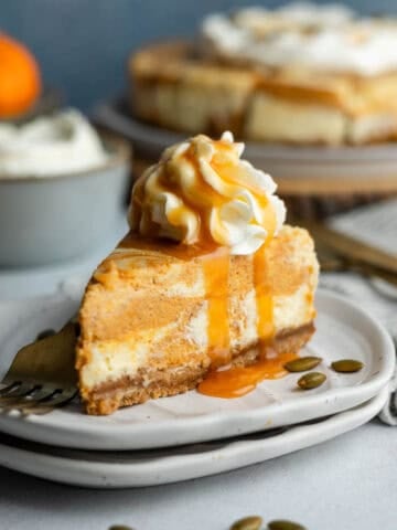 A slice of gluten-free pumpkin swirl cheesecake on a small plate topped with whipped cream and drizzled with caramel sauce.
