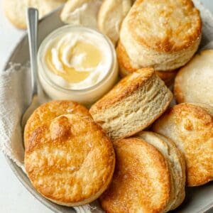 Round gluten free biscuits in bowl next to honey butter.