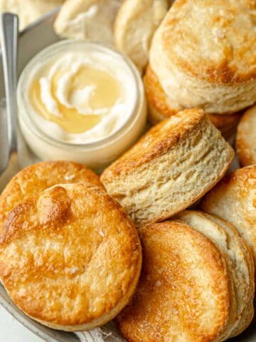 Round gluten free biscuits in bowl next to honey butter.