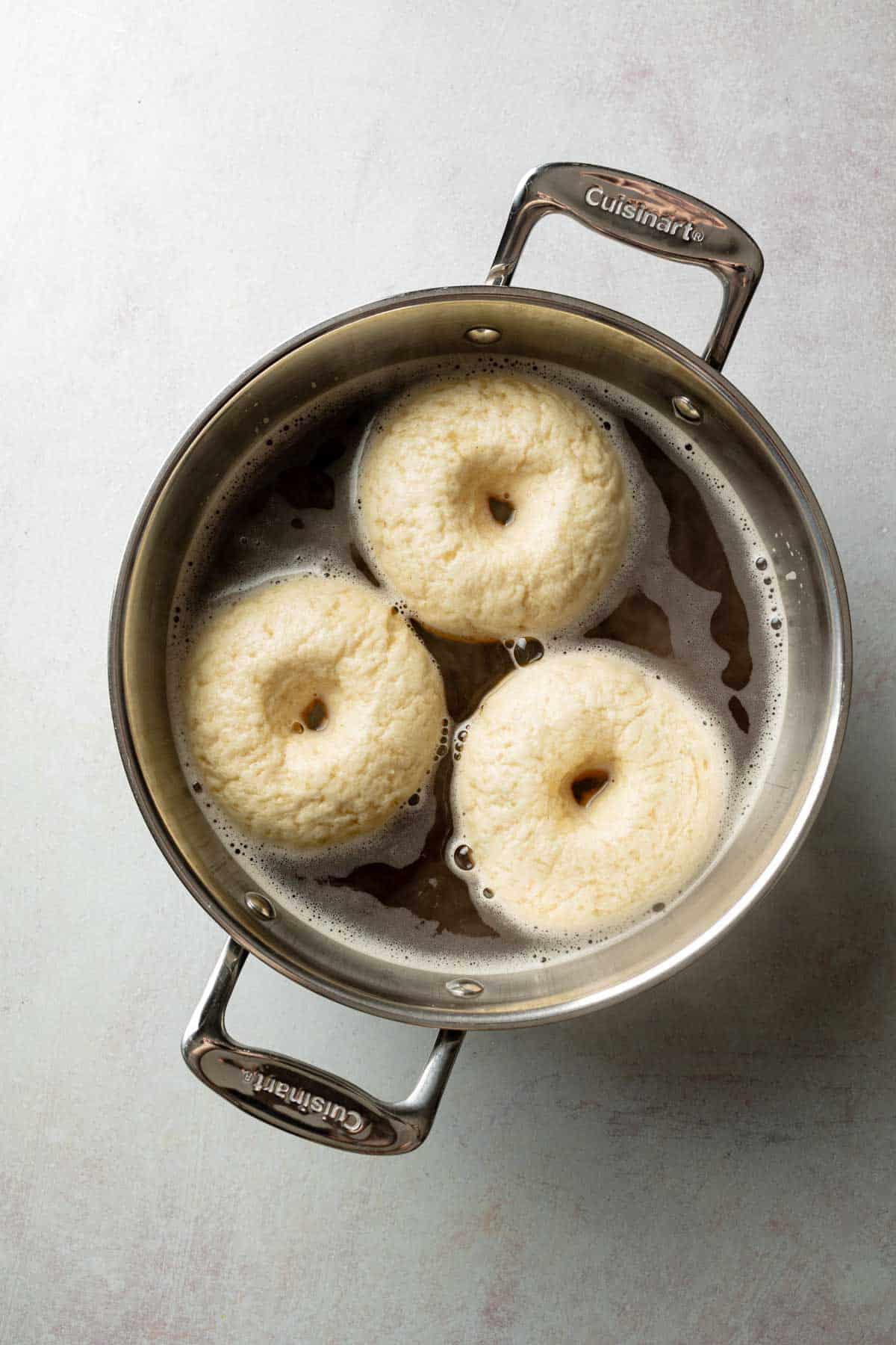 Three gluten-free bagels submerged in a pot of boiling water, puffing up as they cook.