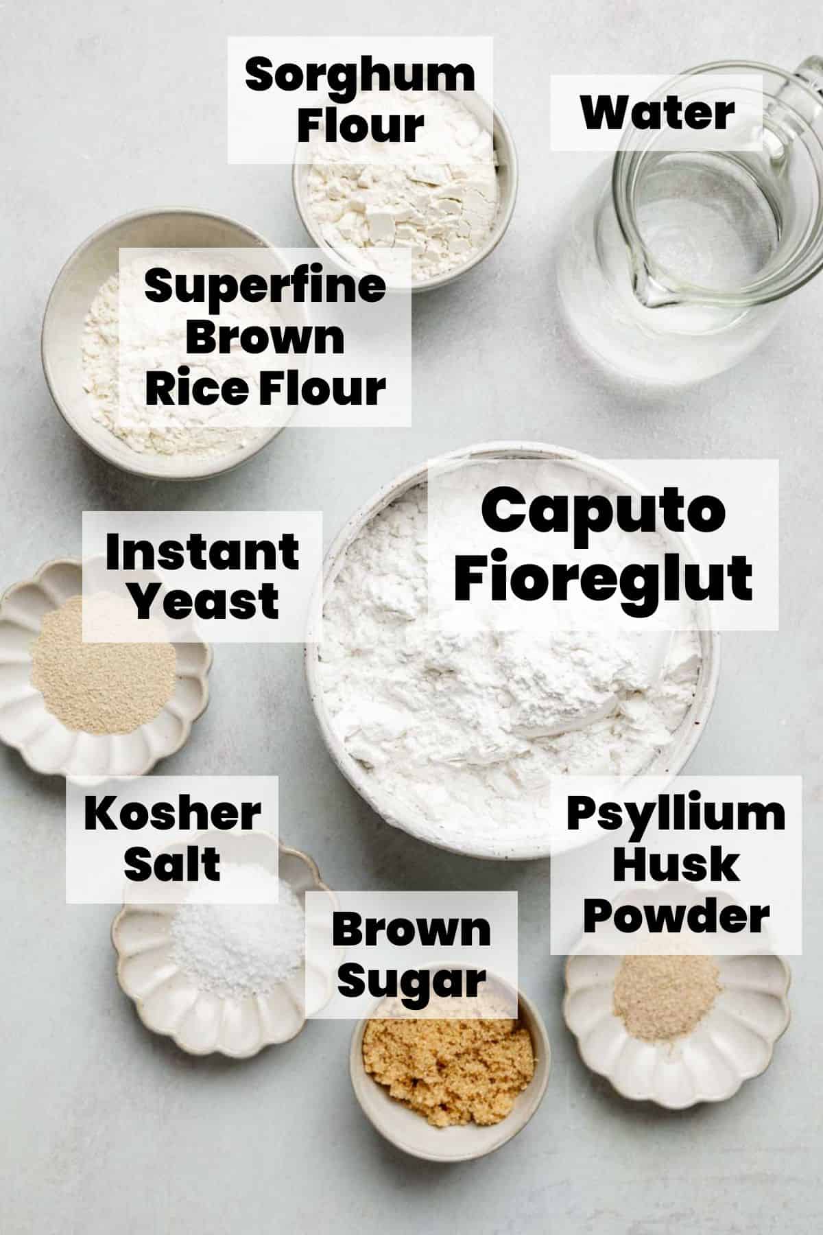 An overhead view of gluten-free bagel ingredients arranged in small bowls, including sorghum flour, brown rice flour, Caputo Fioreglut, psyllium husk powder, instant yeast, kosher salt, brown sugar, and water, with text labels.