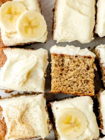 Overhead view of sliced gluten-free banana cake topped with cream cheese frosting, banana slices, and a dusting of cinnamon.