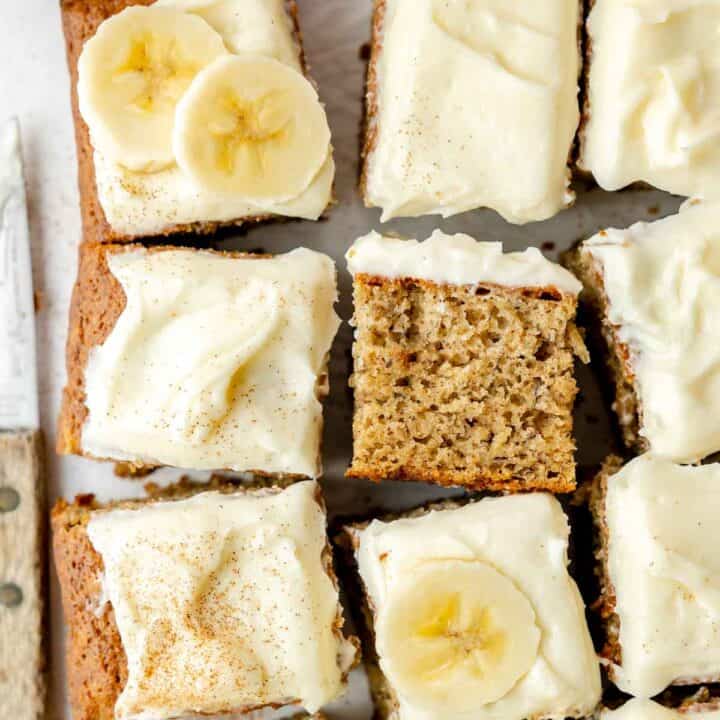 Overhead view of sliced gluten-free banana cake topped with cream cheese frosting, banana slices, and a dusting of cinnamon.