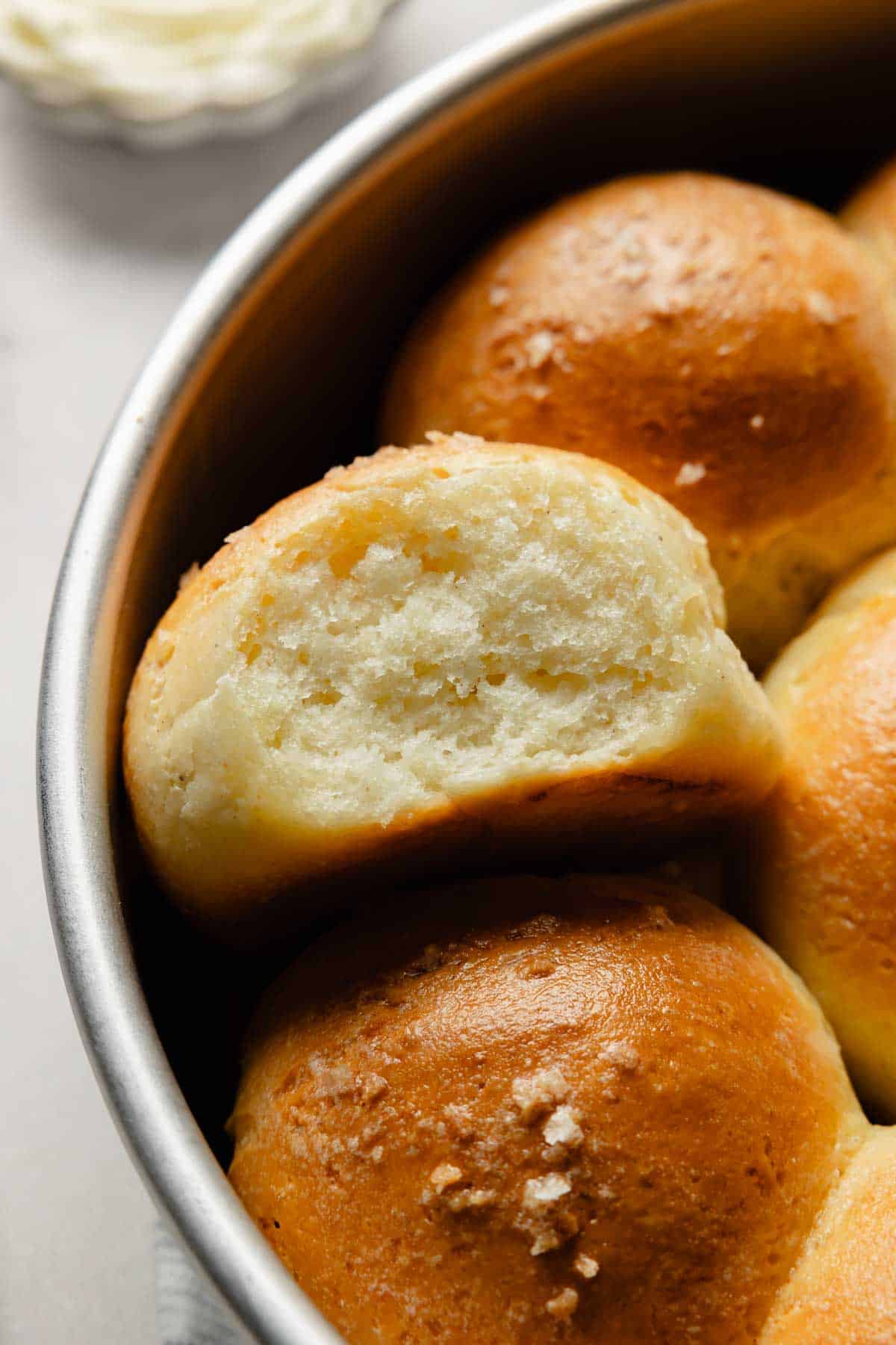 Close-up of a gluten-free dinner roll torn open in the pan, showing the light and fluffy crumb.
