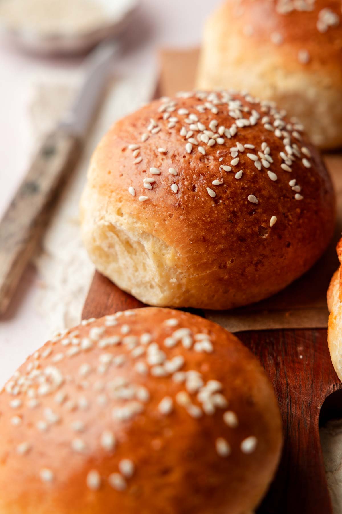 Close-up of soft and golden gluten-free hamburger buns sprinkled with sesame seeds, displayed on a dark wooden board.