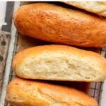 Overhead view of four gluten-free hot dog buns on a cooling rack with parchment paper, two of them cut to reveal a soft and airy crumb.
