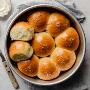Baked gluten-free pull-apart dinner rolls in a round pan, one roll pulled apart to show the fluffy interior.