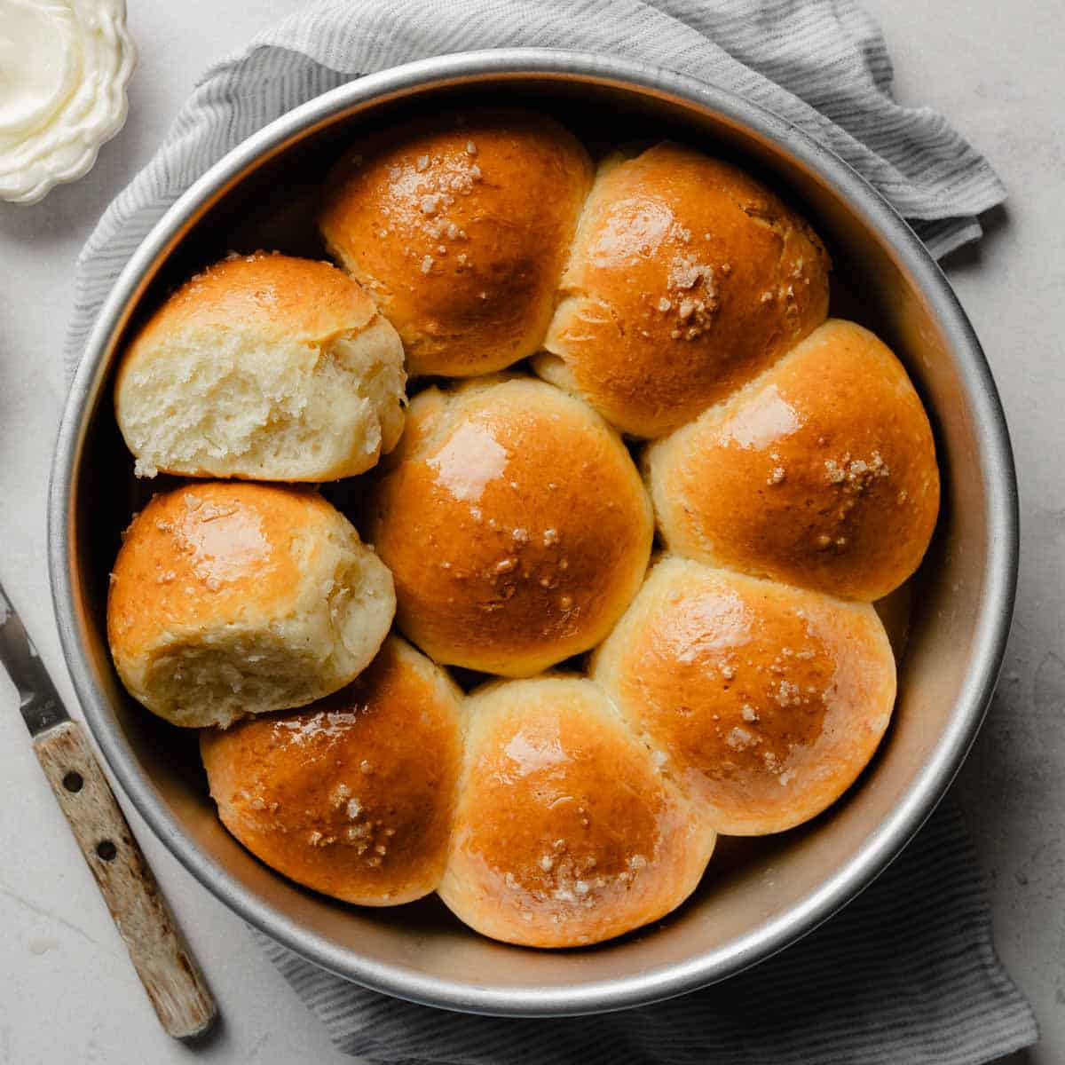 Baked gluten-free pull-apart dinner rolls in a round pan, one roll pulled apart to show the fluffy interior.