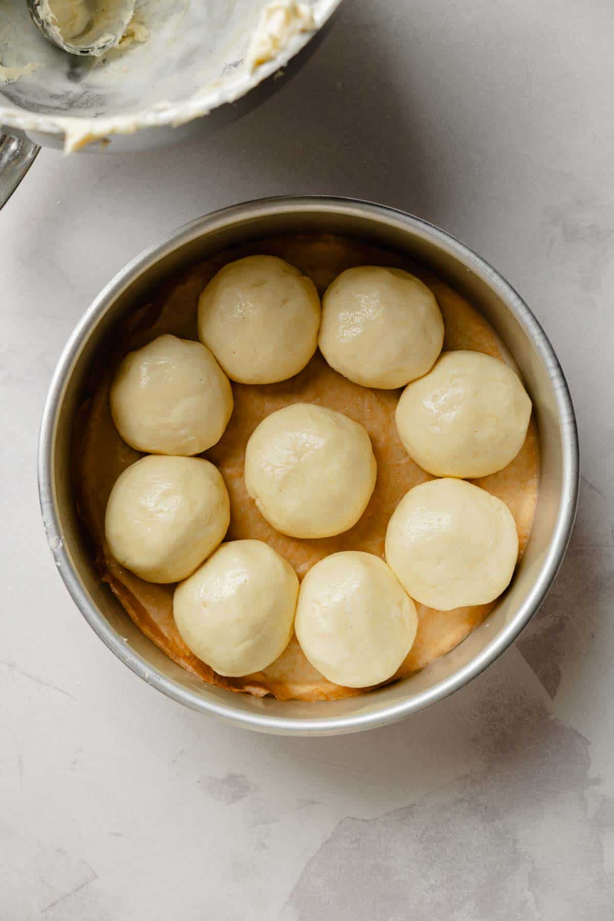 Gluten-free dinner roll dough balls arranged in a round metal pan ready for the first rise.