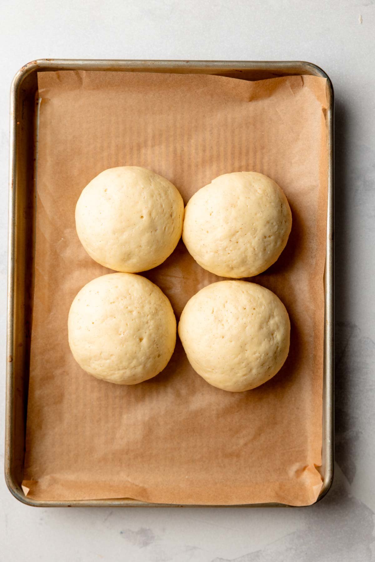 Overhead view of risen gluten-free hamburger buns after proofing on a parchment-lined baking sheet.