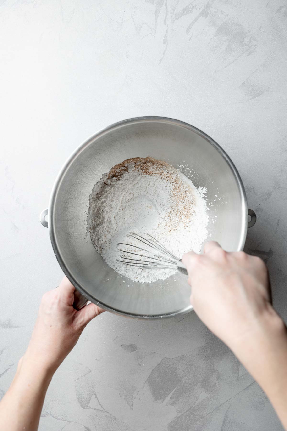 Overhead view of a person whisking dry ingredients in a metal mixing bowl to prepare gluten-free dough.