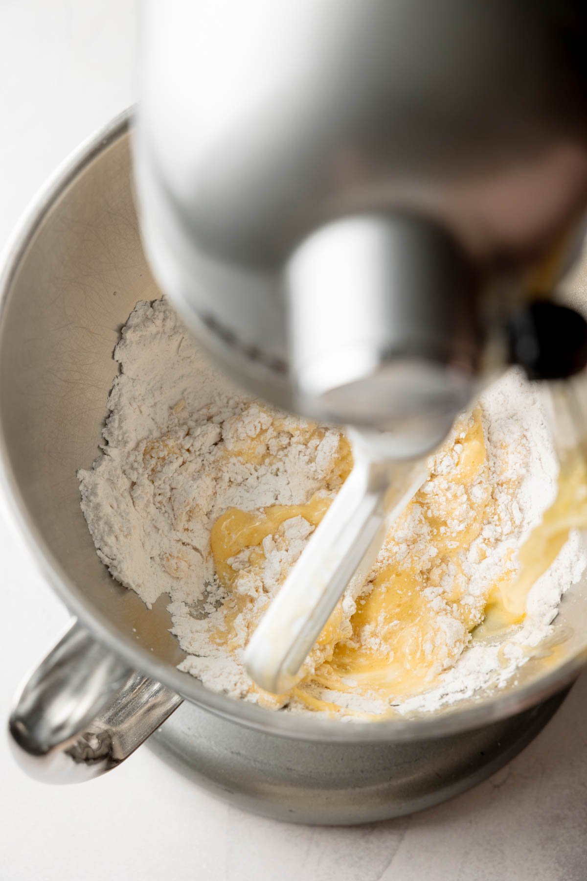 Stand mixer beginning to combine wet and dry ingredients in a metal bowl for gluten-free dough.