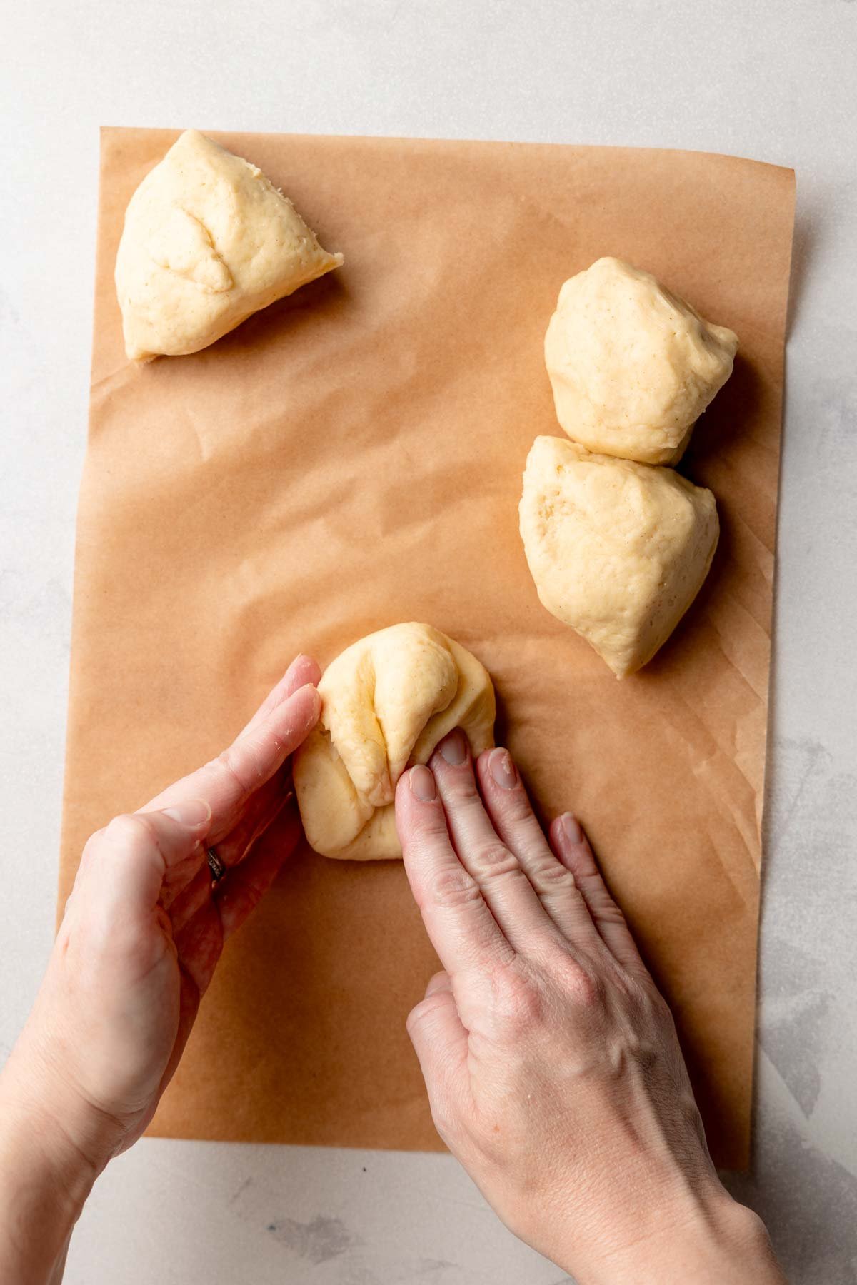 Hands shaping a portion of gluten-free dough into a bun on parchment paper.