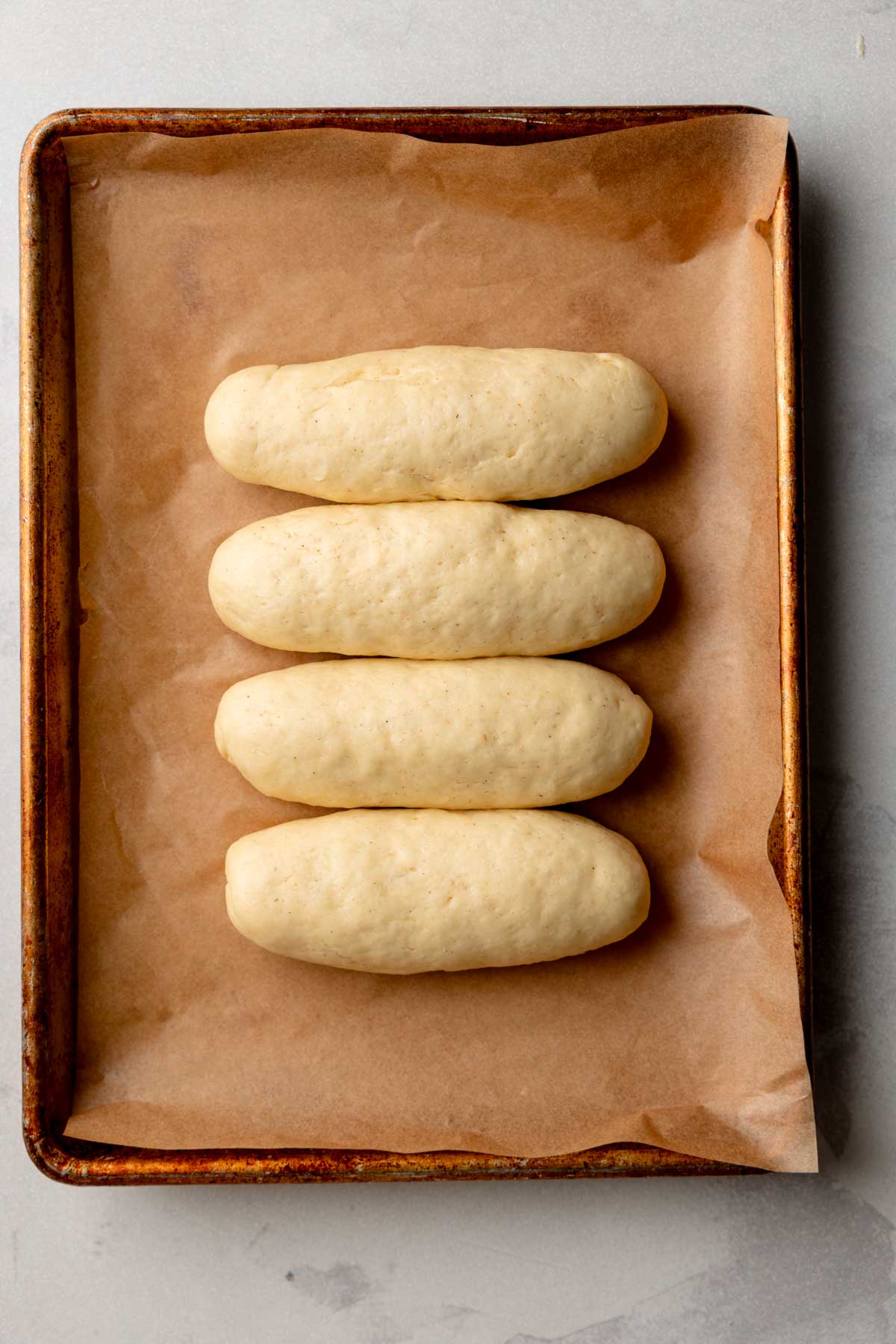 Overhead view of gluten-free hot dog buns after proofing on a baking sheet.