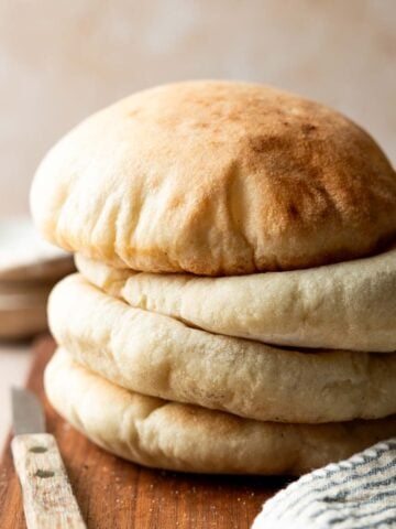A stack of four gluten free pita breads on cutting board next to striped towel and rustic knife.