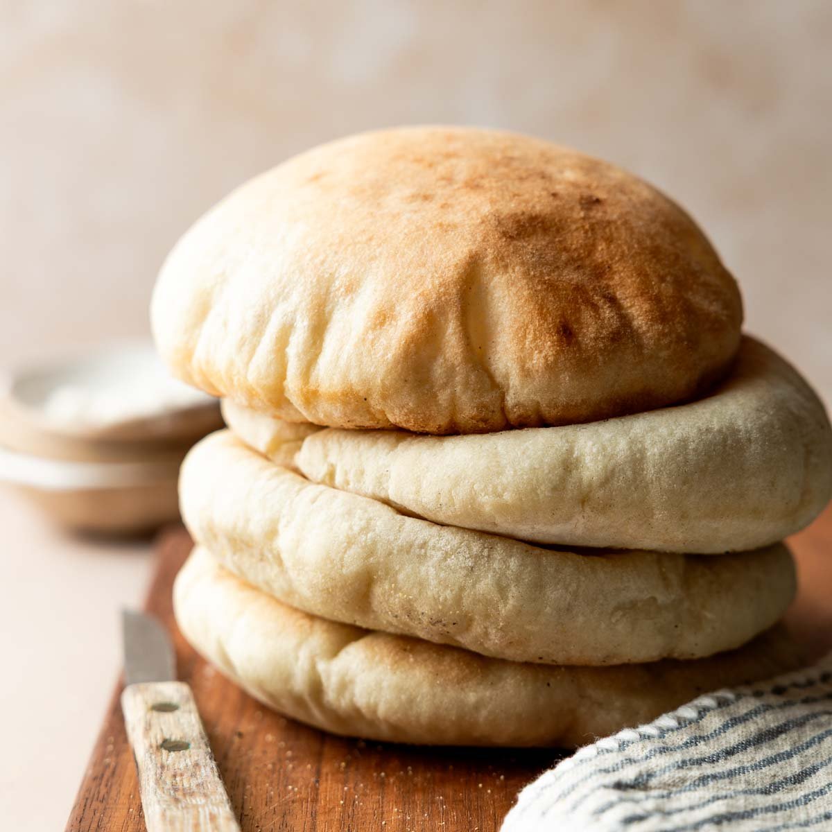A stack of four gluten free pita breads on cutting board next to striped towel and rustic knife.