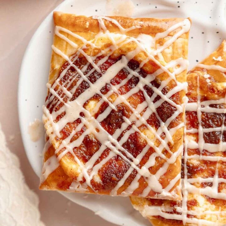Close-up of a single pumpkin danish on a white speckled plate. The flaky crust and pumpkin filling are topped with a neat drizzle of icing.