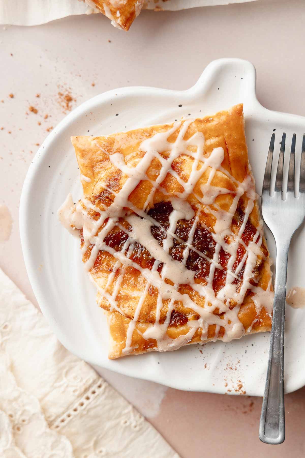 Gluten-free pumpkin danish served on a white plate with a fork. The pastry has a crisp, golden edge and a spiced pumpkin filling with icing drizzled on top.