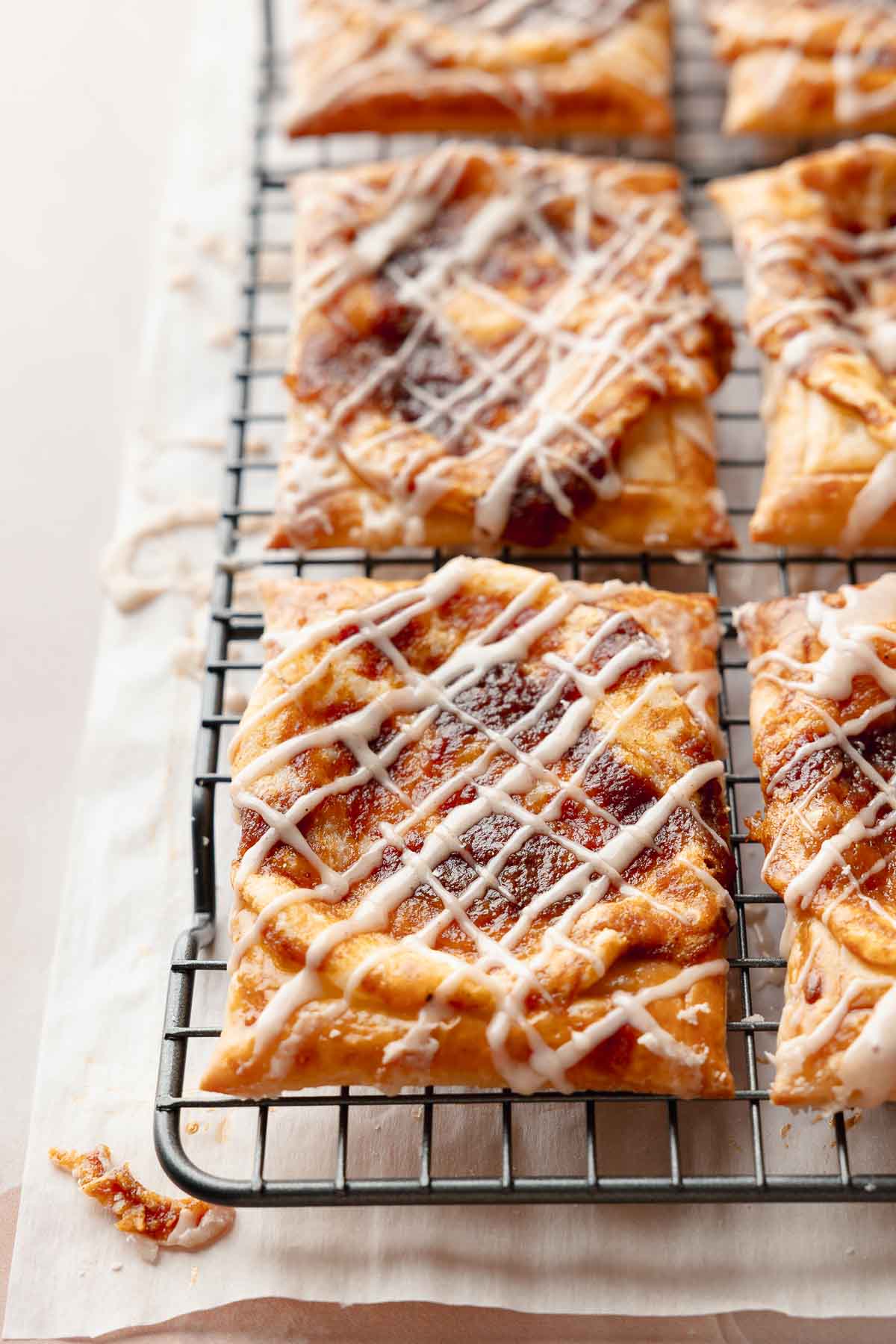 Freshly baked gluten-free pumpkin danishes on a cooling rack. Each one is drizzled with icing and has golden puff pastry with a spiced pumpkin center.