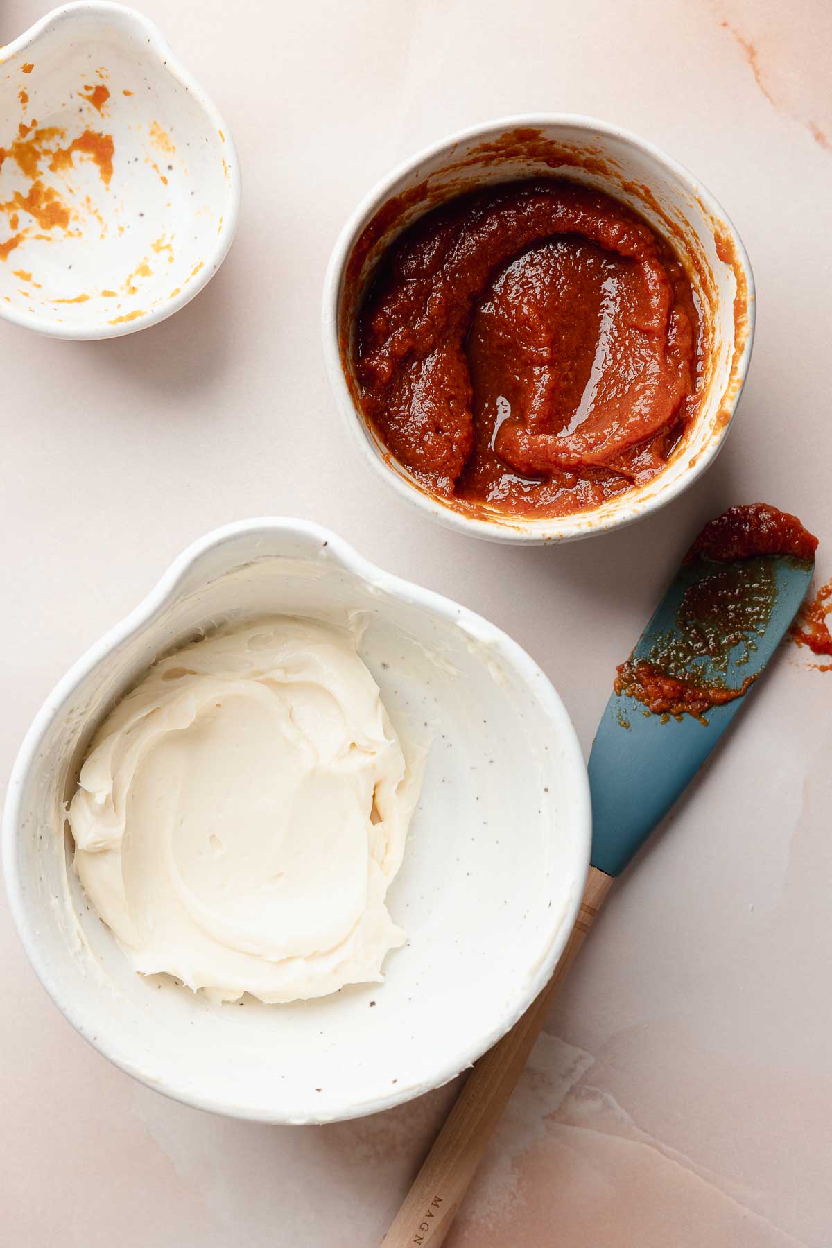 Two bowls with mixed fillings: one with smooth cream cheese filling, the other with spiced pumpkin filling. A spatula with a bit of pumpkin mixture rests beside them.
