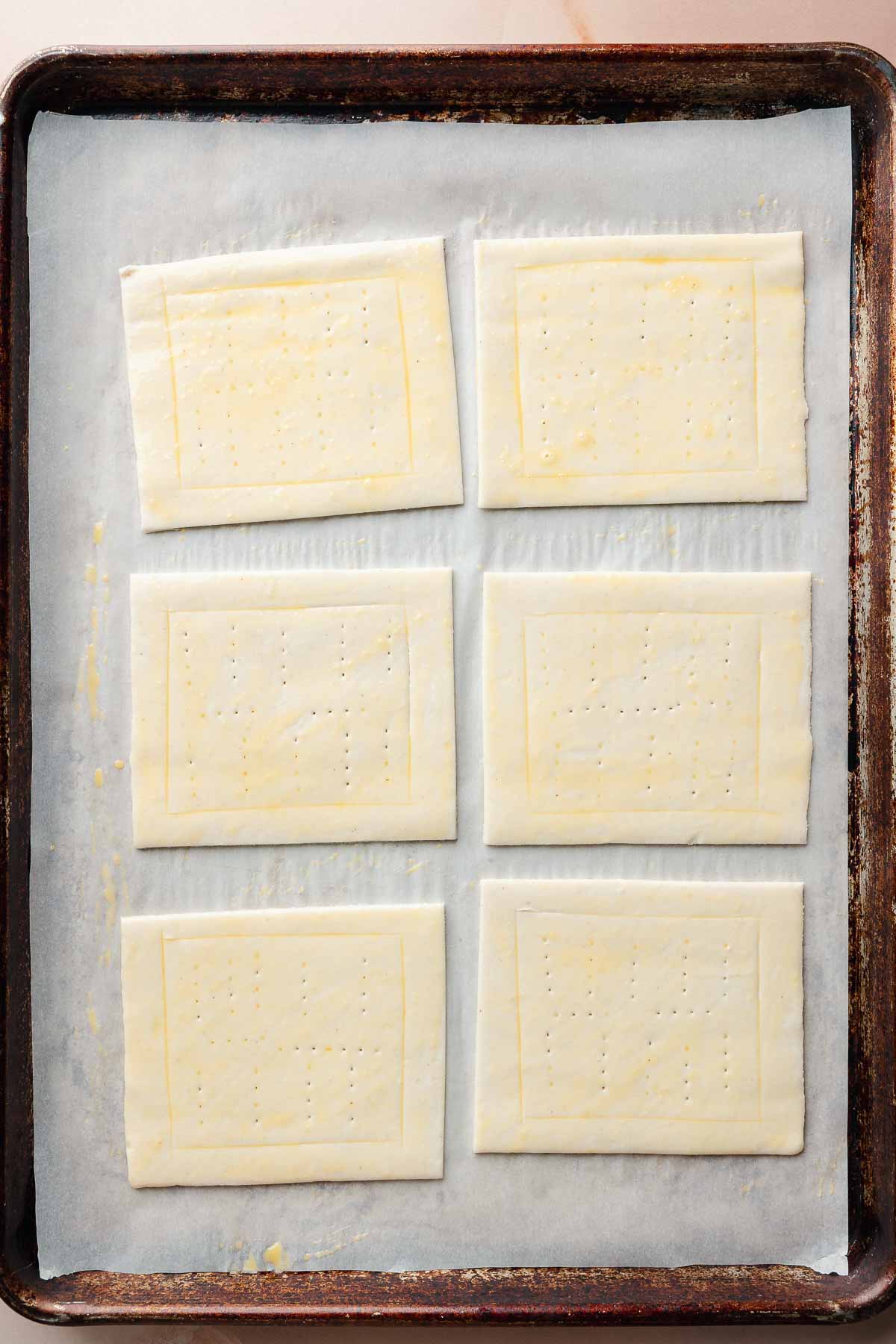 Raw puff pastry rectangles on a baking sheet lined with parchment paper. Each rectangle is scored and docked in the center, and brushed with egg wash.