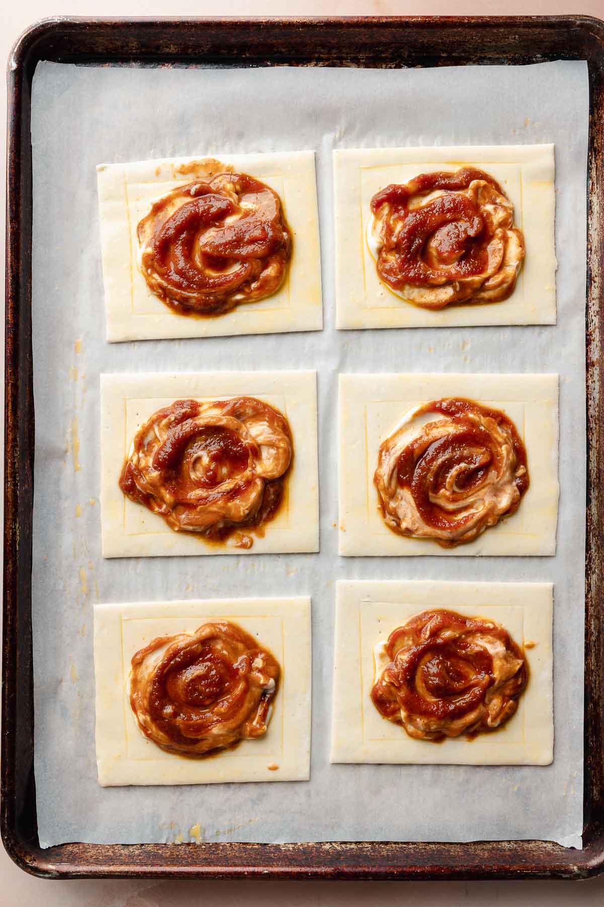 All pastries are filled and ready for baking. The pumpkin and cream cheese filling is swirled in the center of each pastry square.