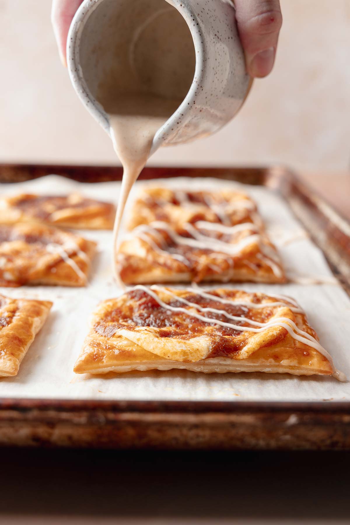 A hand drizzling glaze over freshly baked pumpkin danishes on the tray.