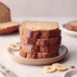 A stack of gluten-free banana bread slices on plate next to banana slices.