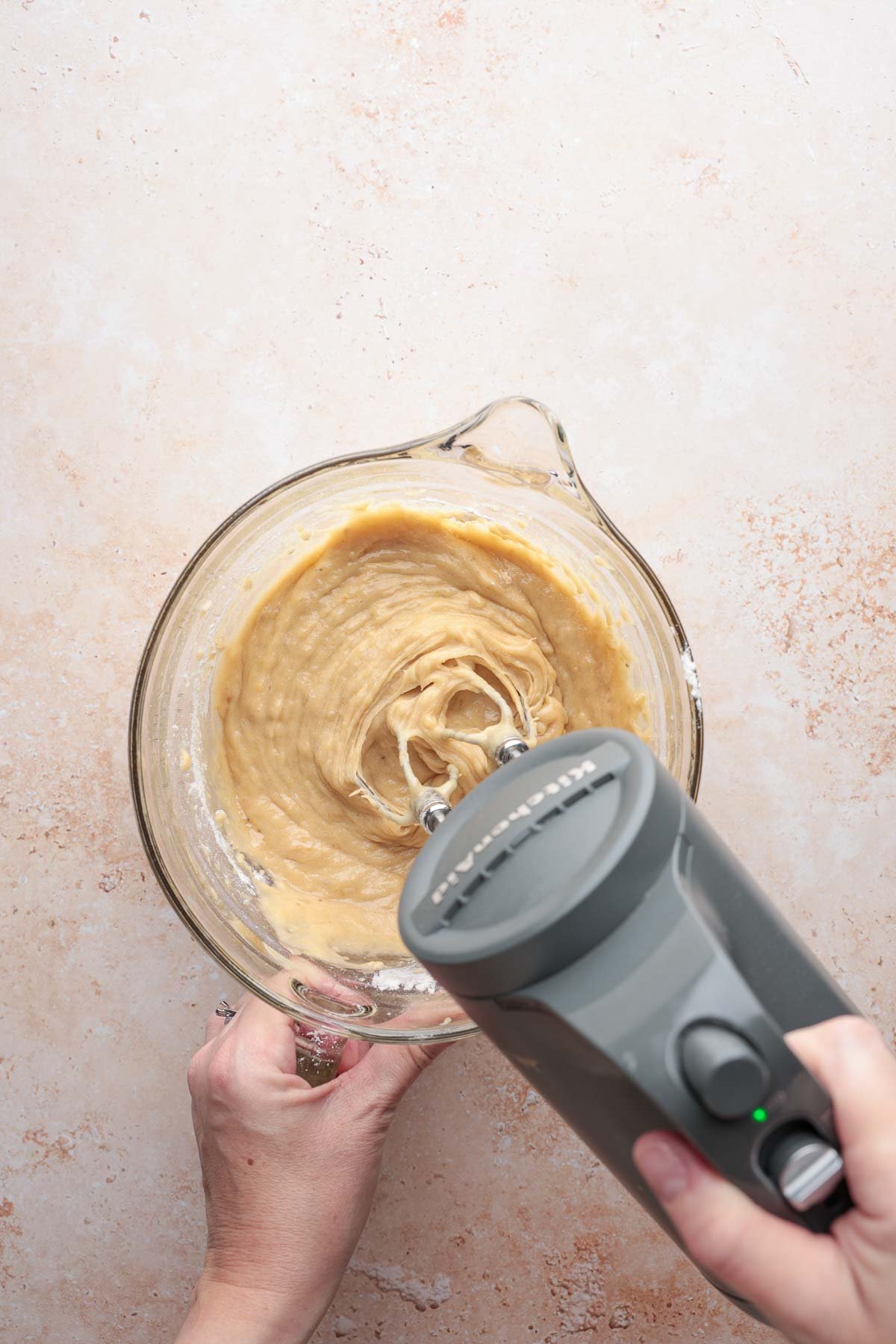 Electric mixer blending banana bread batter in glass bowl.