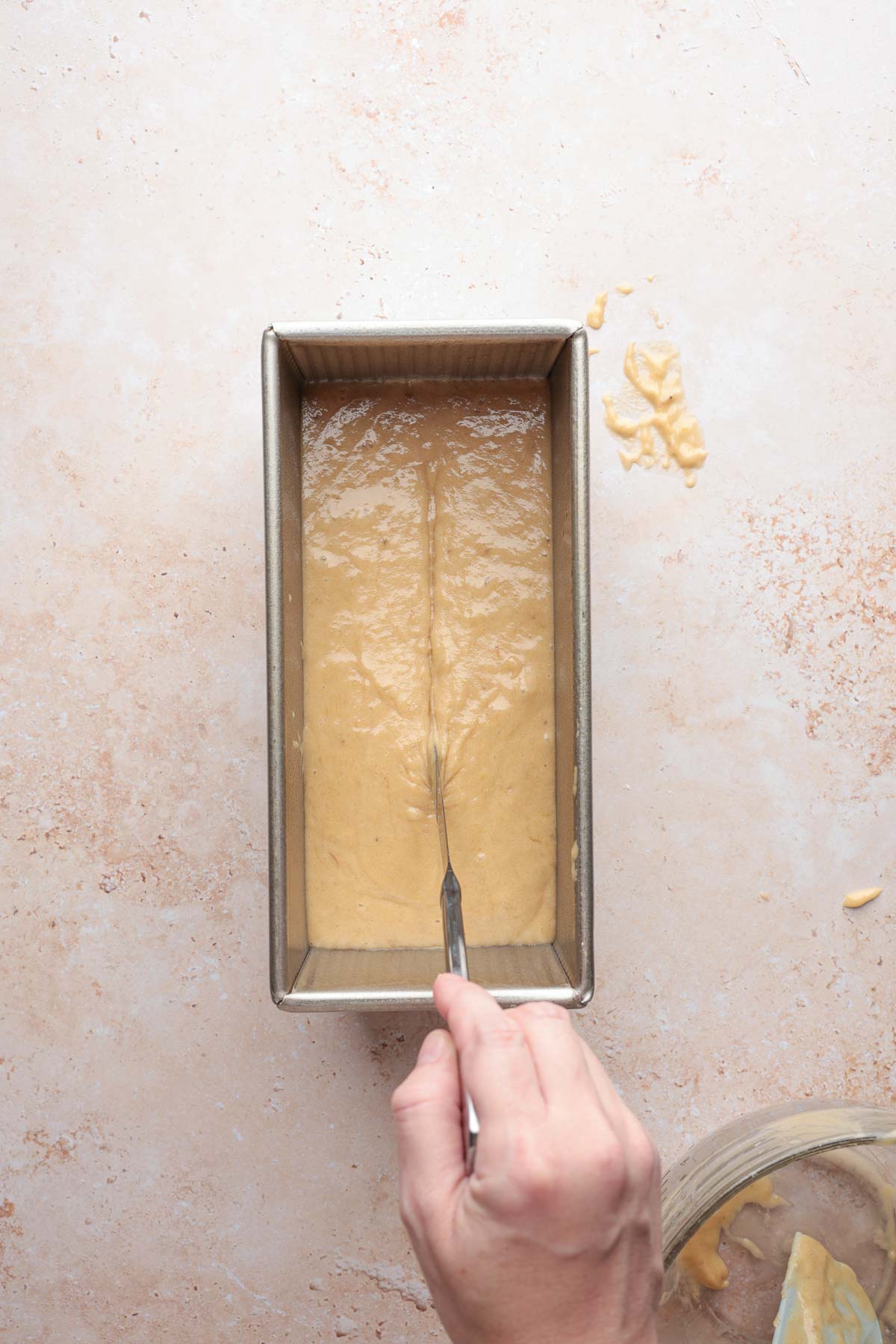Batter poured into loaf pan being scored with knife.