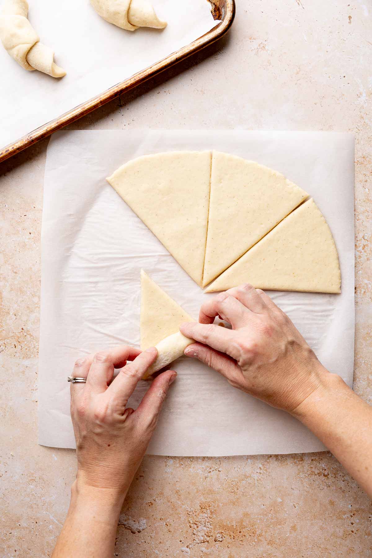 Hands rolling gluten-free crescent roll dough triangle on parchment paper.