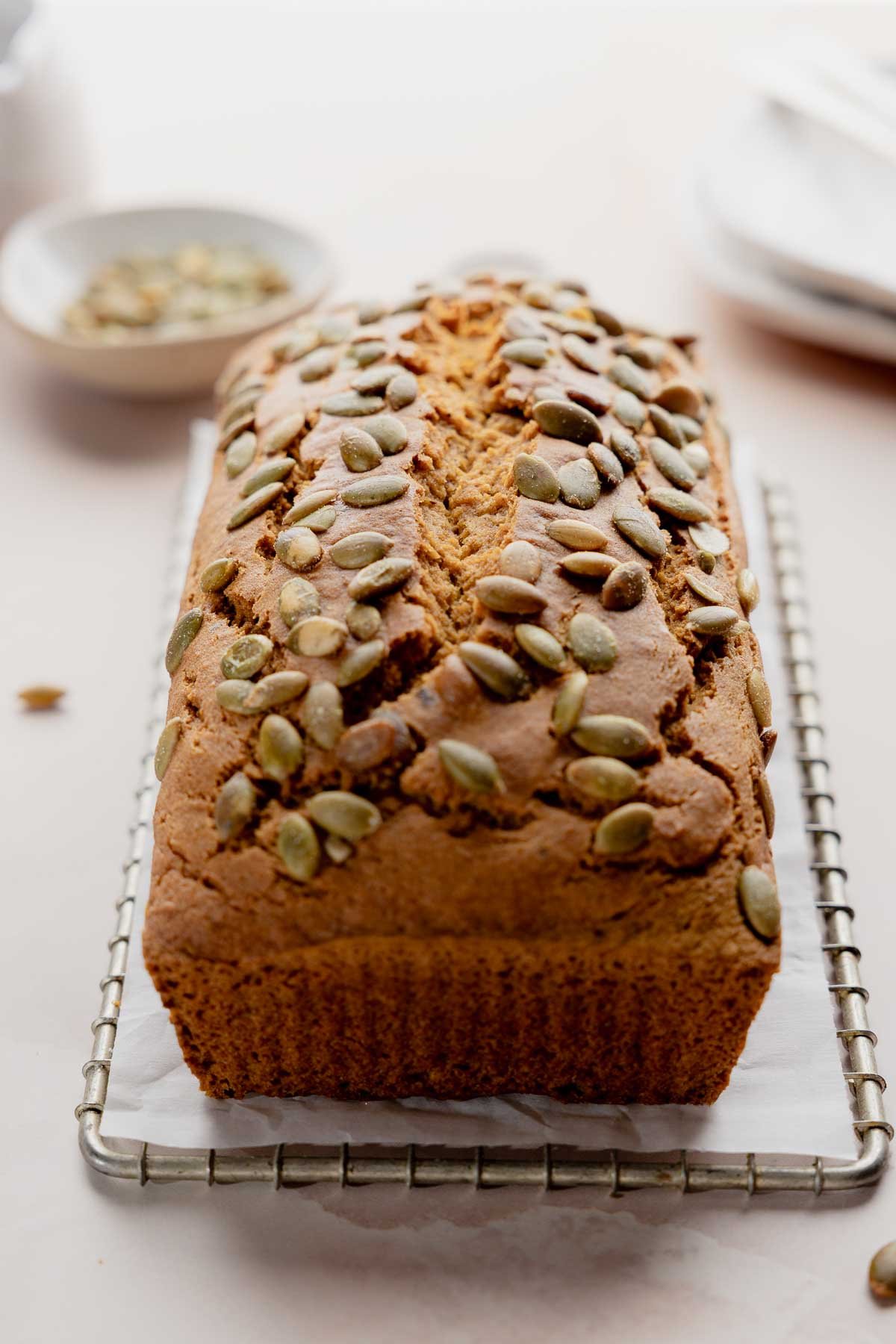 Baked gluten free pumpkin bread loaf topped with pumpkin seeds on cooling rack.