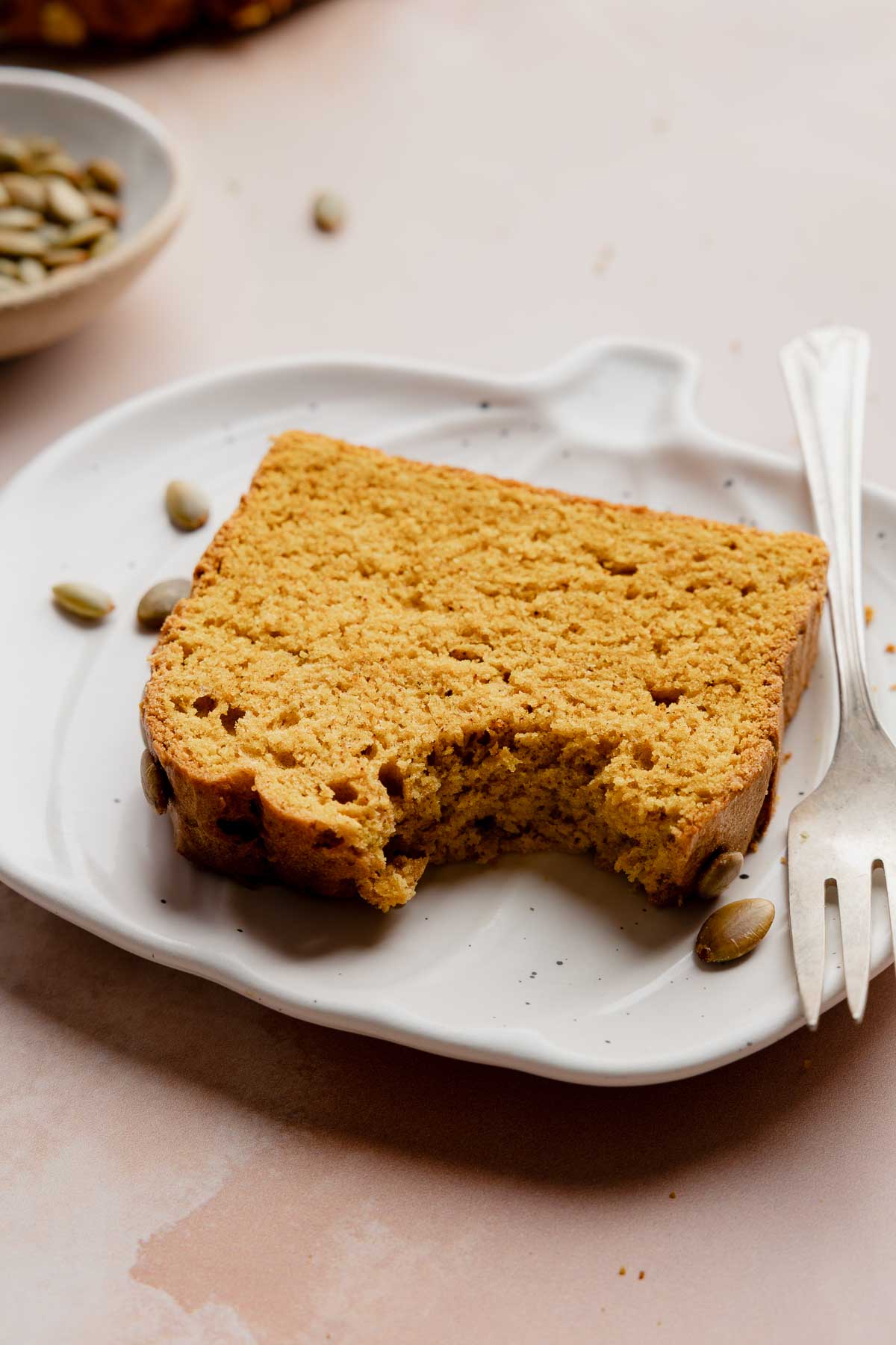 Slice of gluten free pumpkin bread with a bite taken out on white plate with fork.
