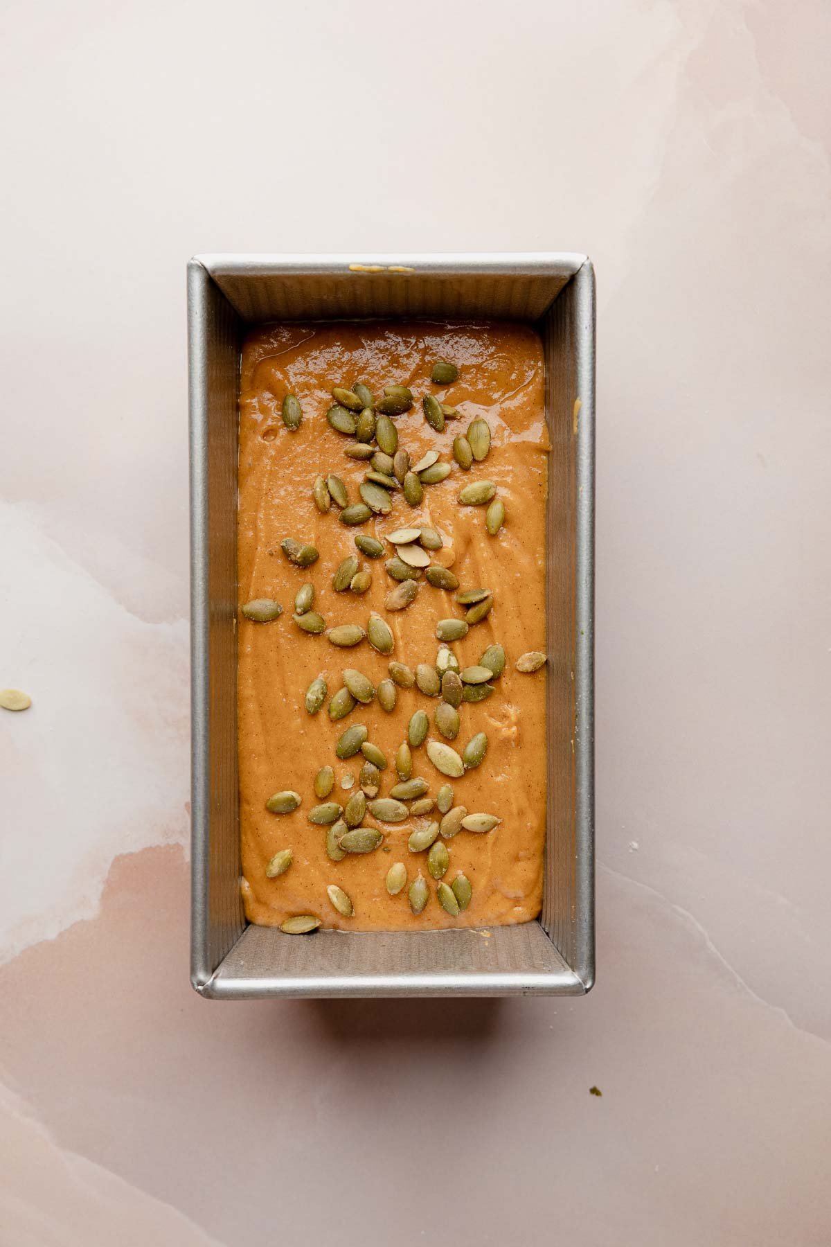Gluten free pumpkin bread batter in loaf pan topped with pumpkin seeds.