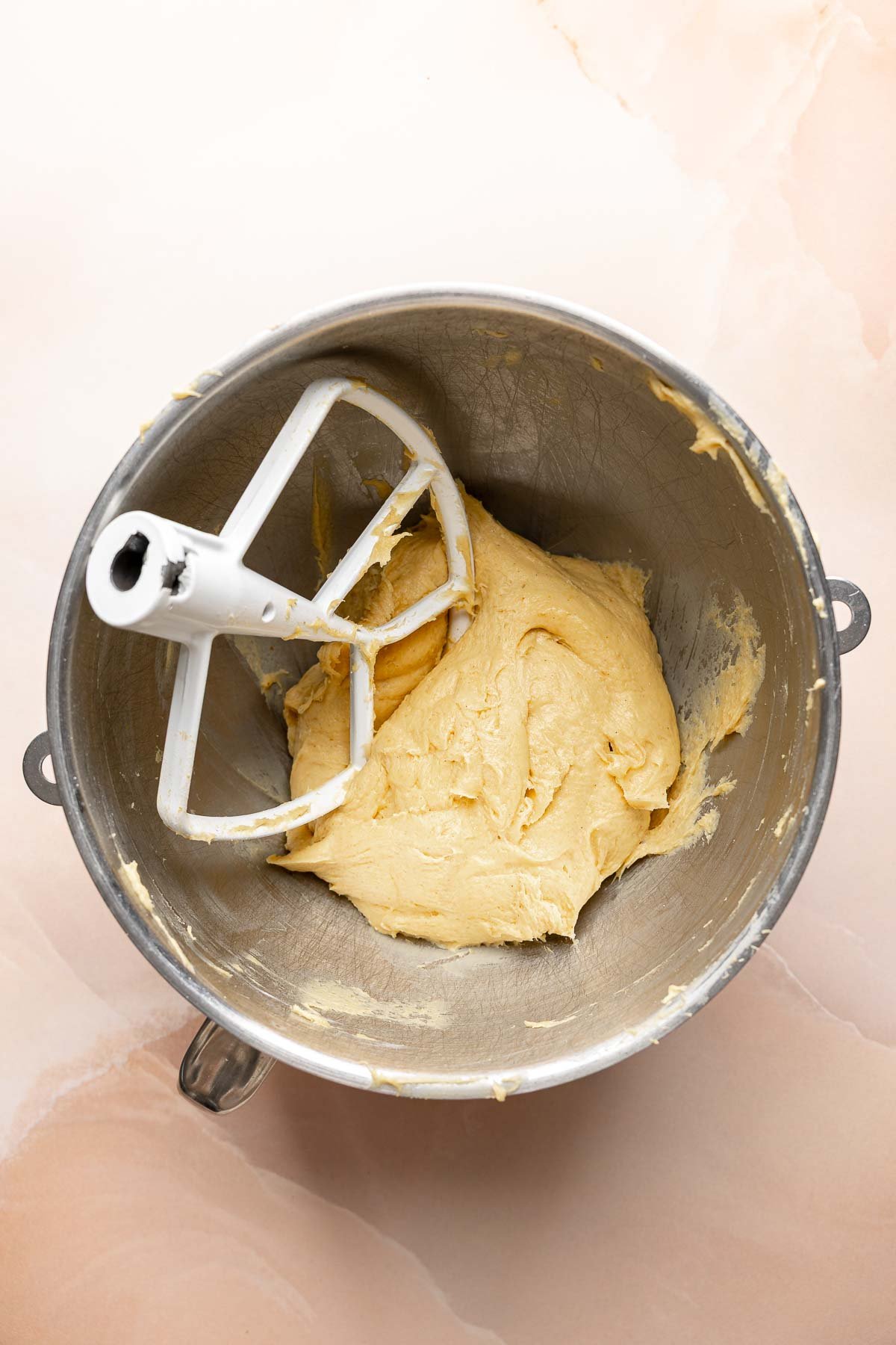 Pumpkin dough in center of mixing bowl with paddle attachment resting to the side.