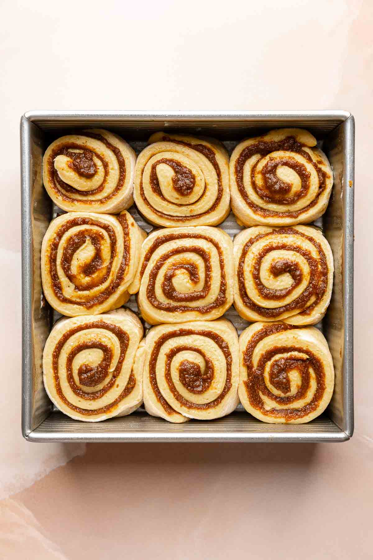 Pumpkin cinnamon rolls after rise, more puffed, nestled in pan.