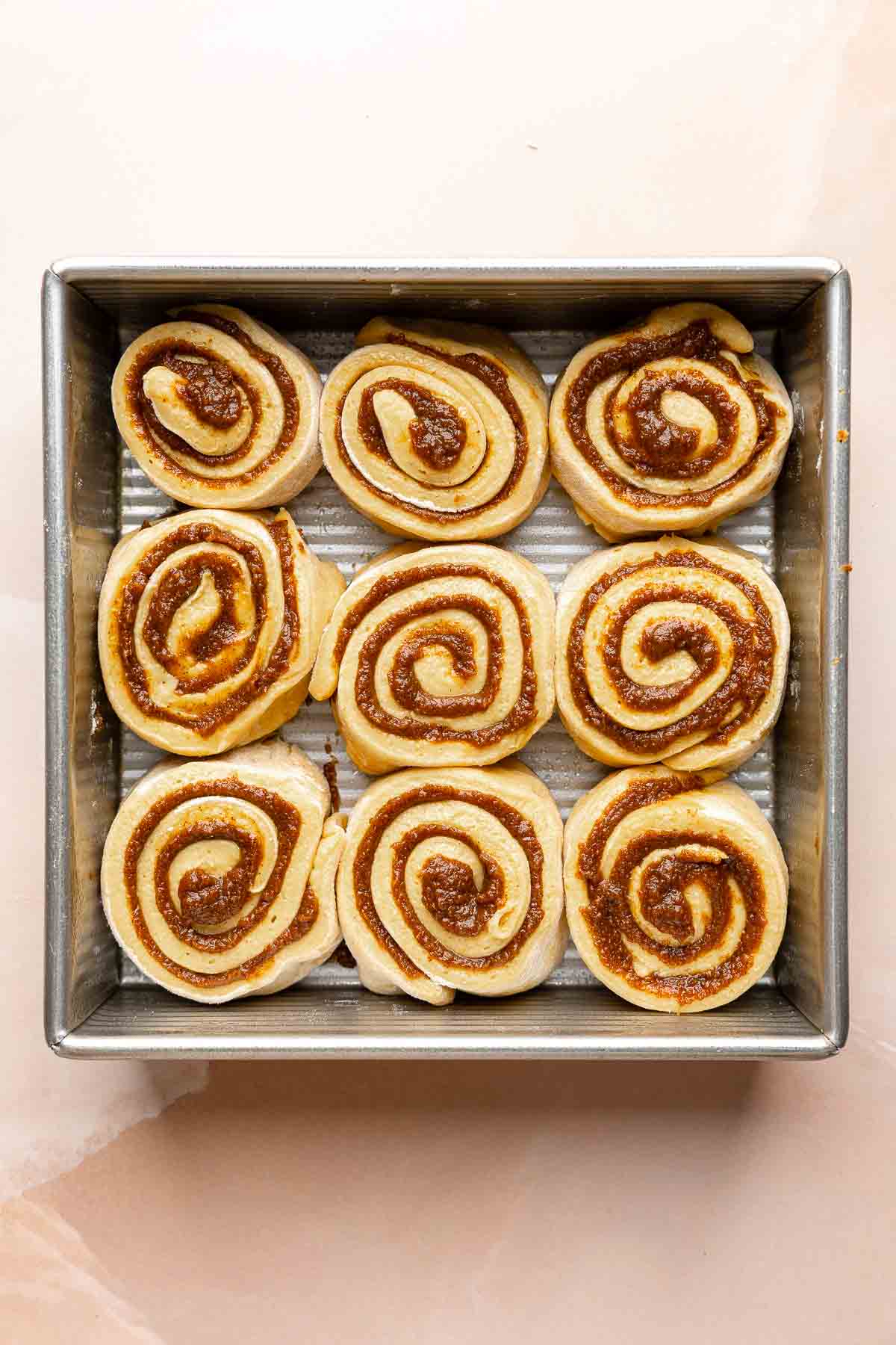 Pumpkin cinnamon rolls before rise, nestled in square pan.