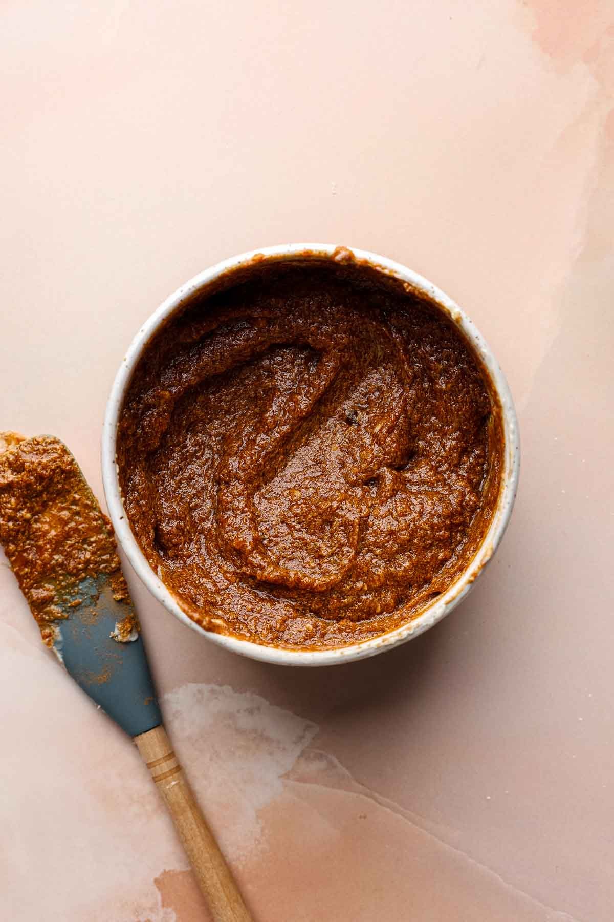 Pumpkin filling mixed in small bowl next to blue spatula with filling on it.