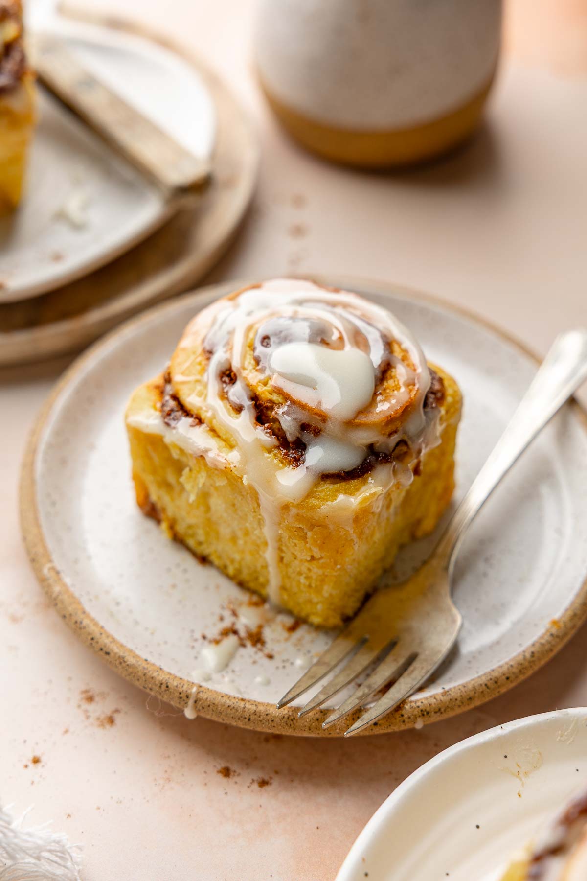Single iced pumpkin cinnamon roll on plate with fork.