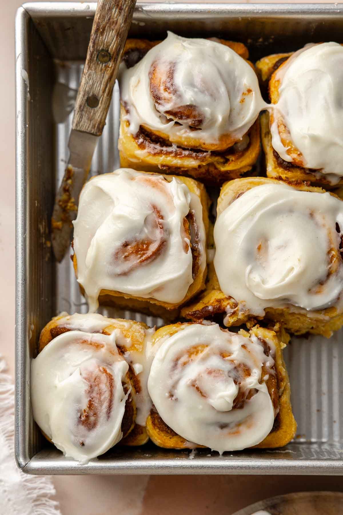 Gluten free pumpkin cinnamon rolls in baking pan topped with thick cream cheese frosting.