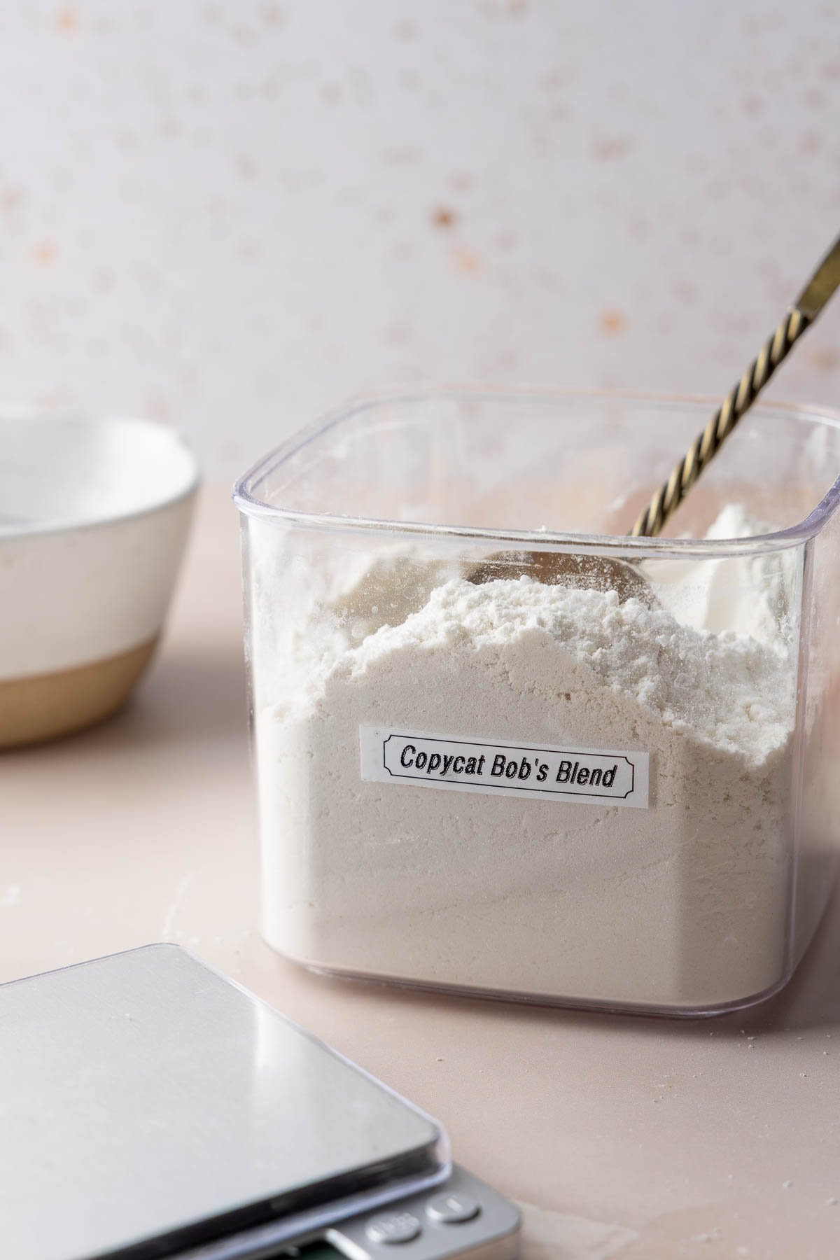 Container labeled &ldquo;Copycat Bob&rsquo;s Blend&rdquo; filled with gluten-free flour mixture and a metal scoop.