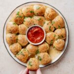Gluten-free cheesy garlic pull apart bread wreath with marinara dipping sauce in center.